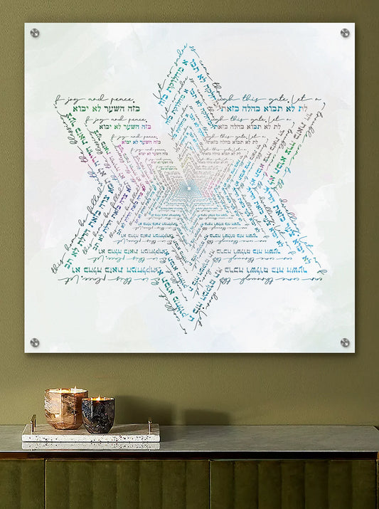 A square wall art print mounted on a wall above a console table. The print features a large Star of David composed of layered, swirling handwritten text in shades of blue, green, pink, and purple on a white background with the text of the Birkat Habayit text.