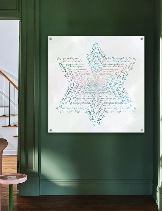 A square wall art print featuring a large multicolored Star of David made from script text, mounted on a dark green wall in an interior room with a staircase and wood floor visible. A birkat habayit.