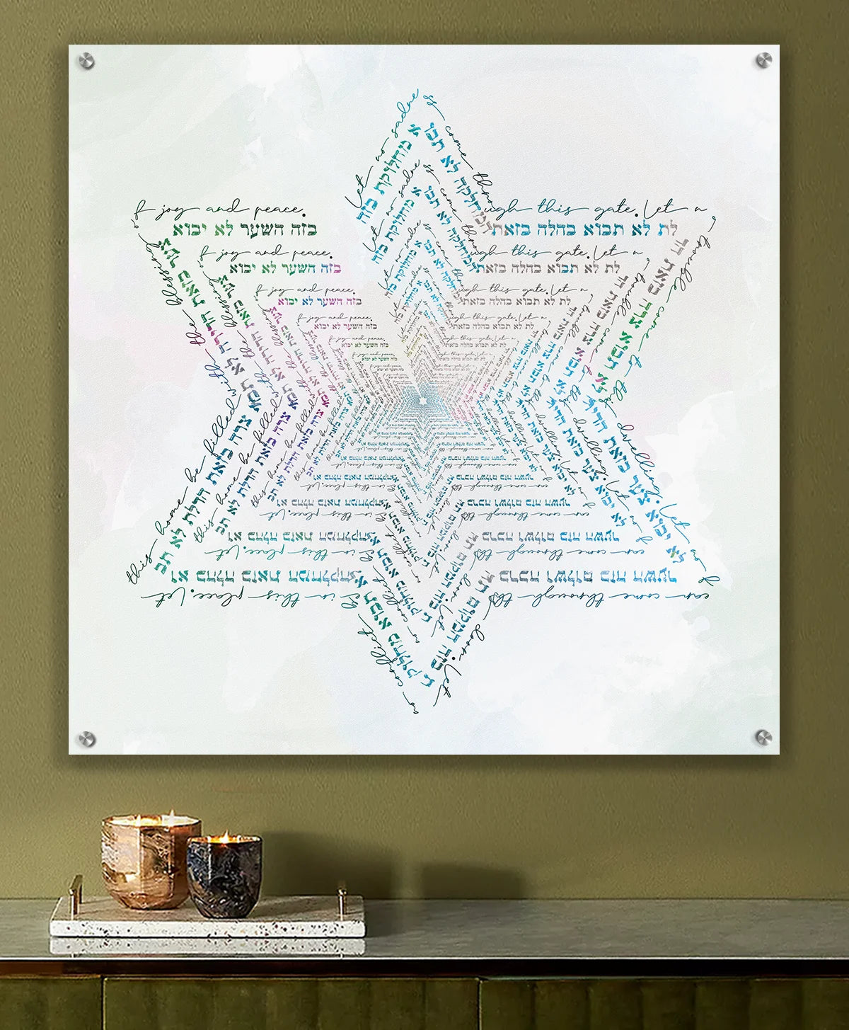 A square wall art print mounted on a wall above a console table. The print features a large Star of David composed of layered, swirling handwritten text in shades of blue, green, pink, and purple on a white background with the text of the Birkat Habayit text.