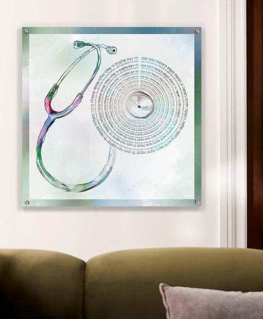 A square wall art print hanging above a sofa, featuring a stylized stethoscope and circular text design of the hebrew Physician's Prayer in pastel rainbow tones on a white background.